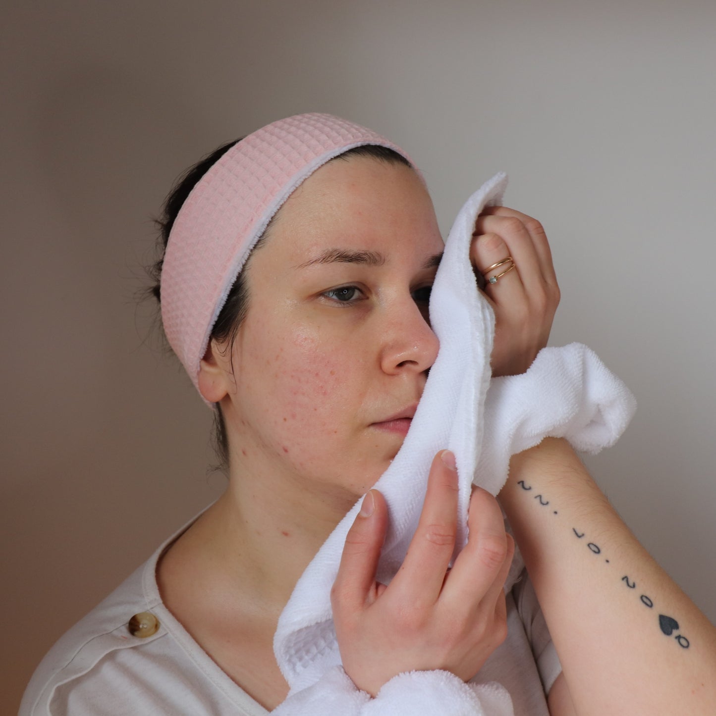 femme avec bandeau de soin rose utilisant une serviette visage douce en éponge bambou de couleur blanche.