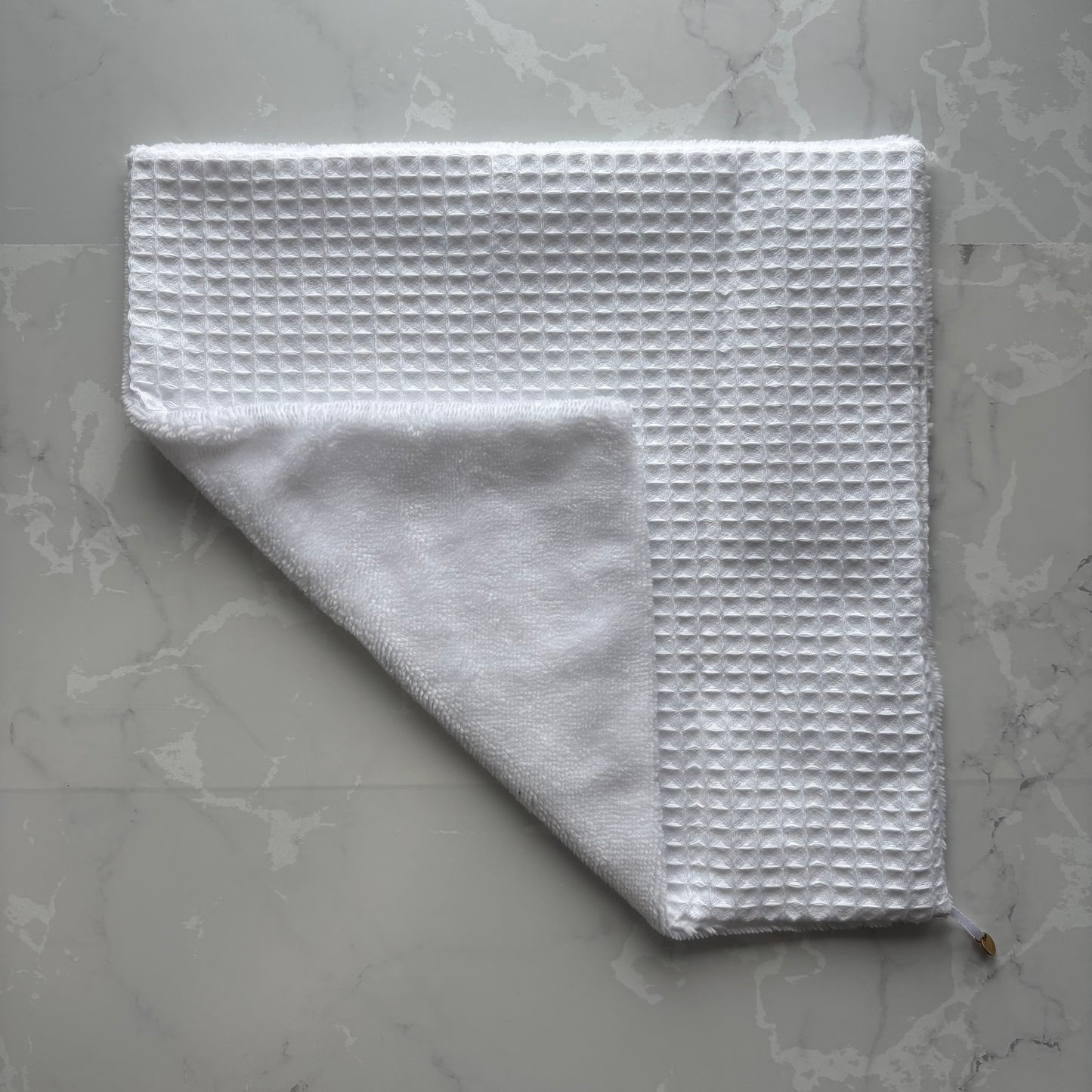 serviette visage posé à plat en éponge bambou et nid d'abeille blanc avec un logo médaillon.