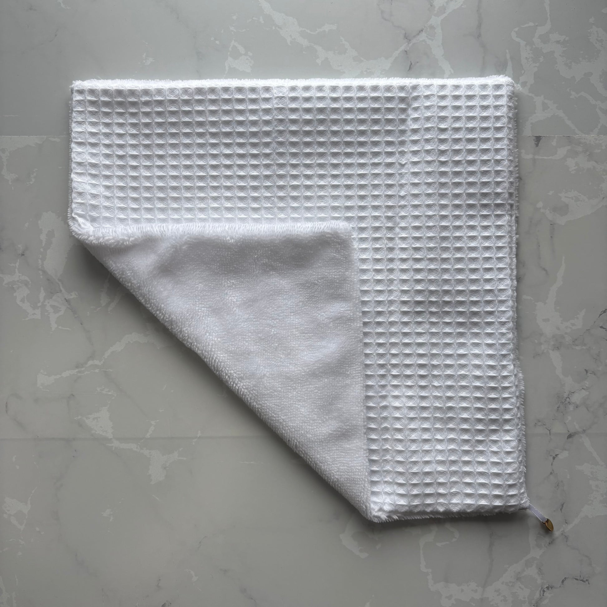 serviette visage posé à plat en éponge bambou et nid d'abeille blanc avec un logo médaillon.
