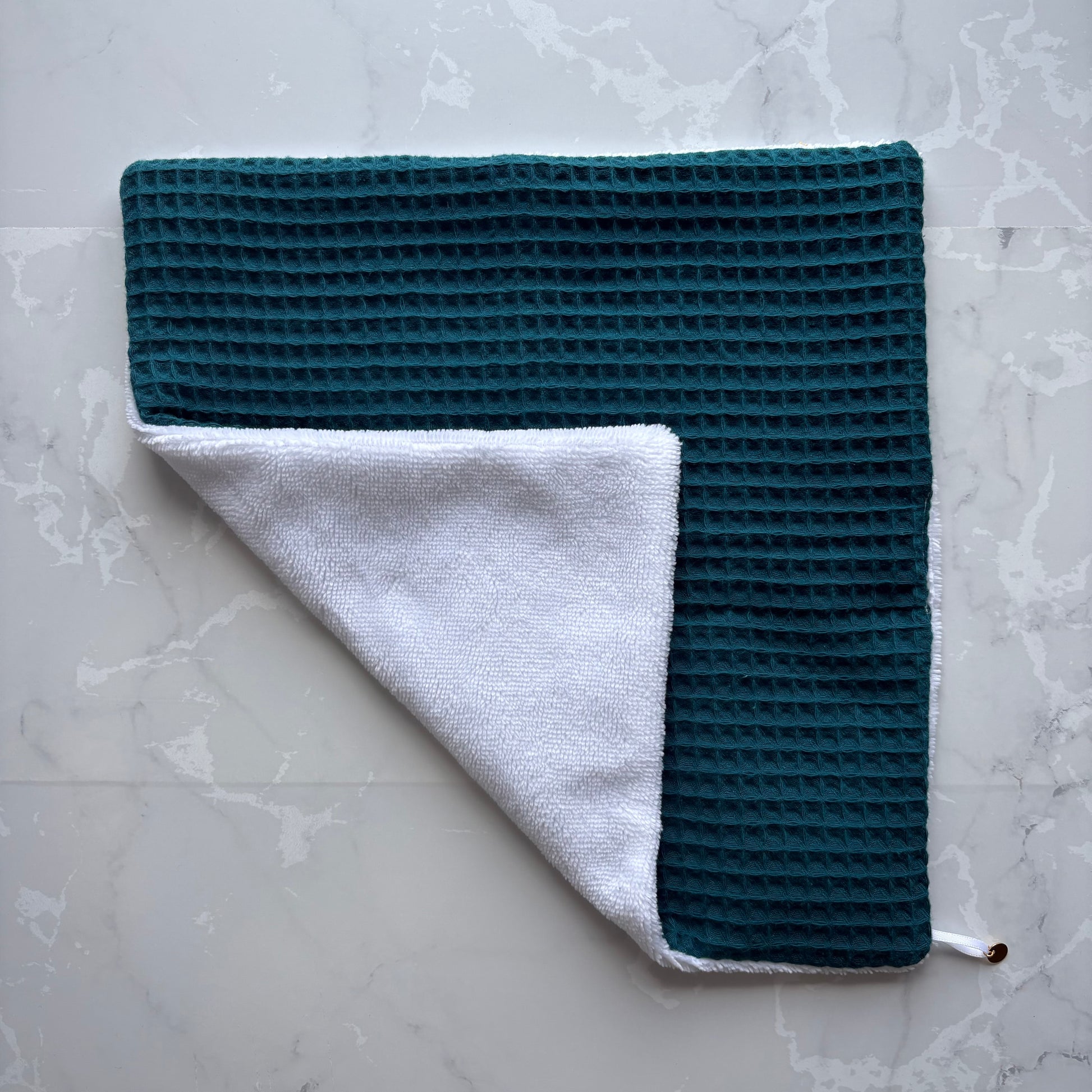 serviette visage posé à plat en  éponge bambou blanc et nid d'abeille bleu carnard avec un logo médaillon.