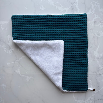 serviette visage posé à plat en  éponge bambou blanc et nid d'abeille bleu carnard avec un logo médaillon.