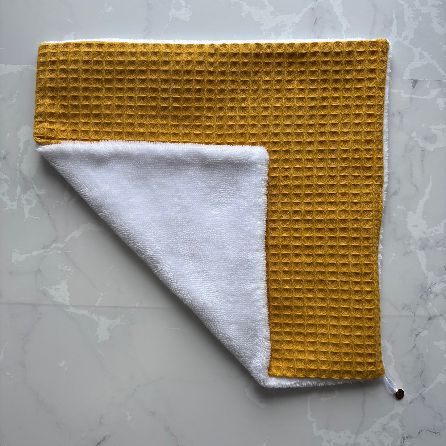 serviette visage posé à plat en éponge bambou blanc et nid d'abeille moutarde avec un logo médaillon.