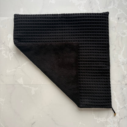 serviette visage posé à plat en éponge bambou et nid d'abeille noir avec un logo médaillon.