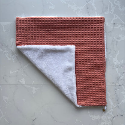 serviette visage posé à plat en éponge bambou blanc et nid d'abeille terracotta avec un logo médaillon.